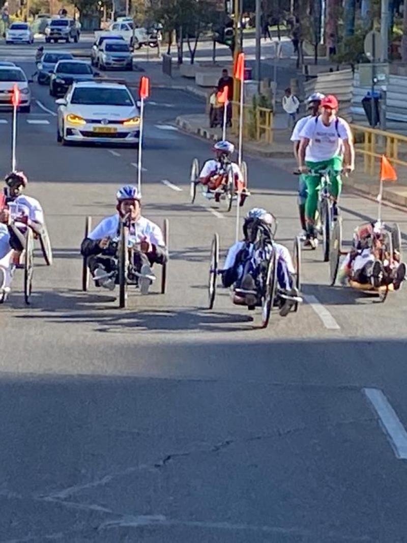 Six handcyclists ride through the city centre in Windhoek with cars following behind.